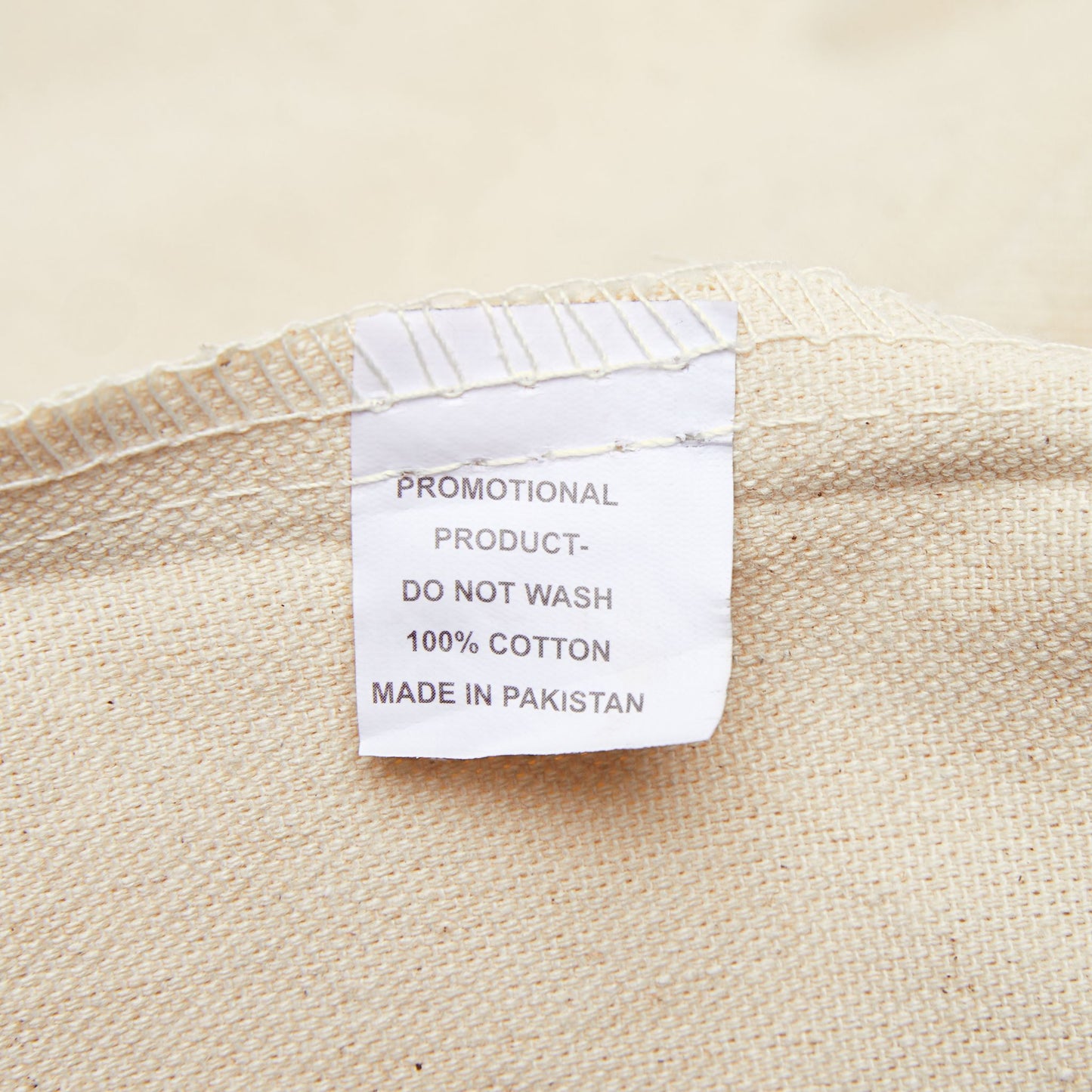 Close-up of the tote bag's care label showing 100% cotton, promotional product, do not wash