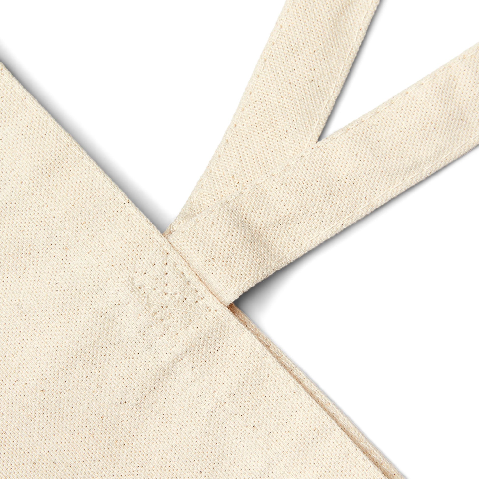 Close-up of the natural cotton canvas tote bag's stitched handle and strap seam