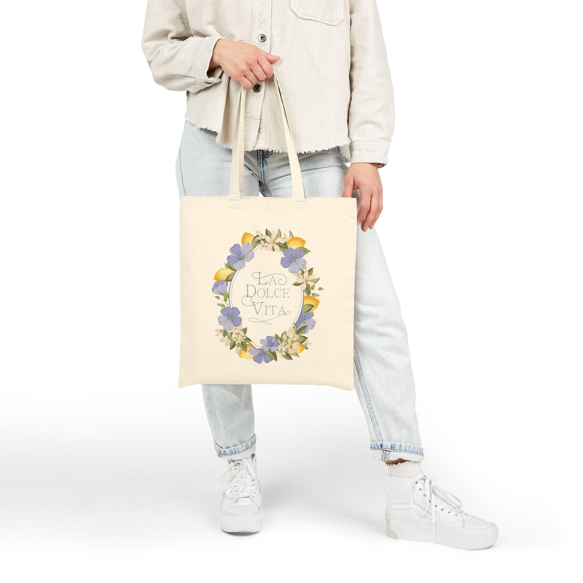 Model in denim and a cream shirt holding the lemon and violet floral canvas tote bag, full-body view