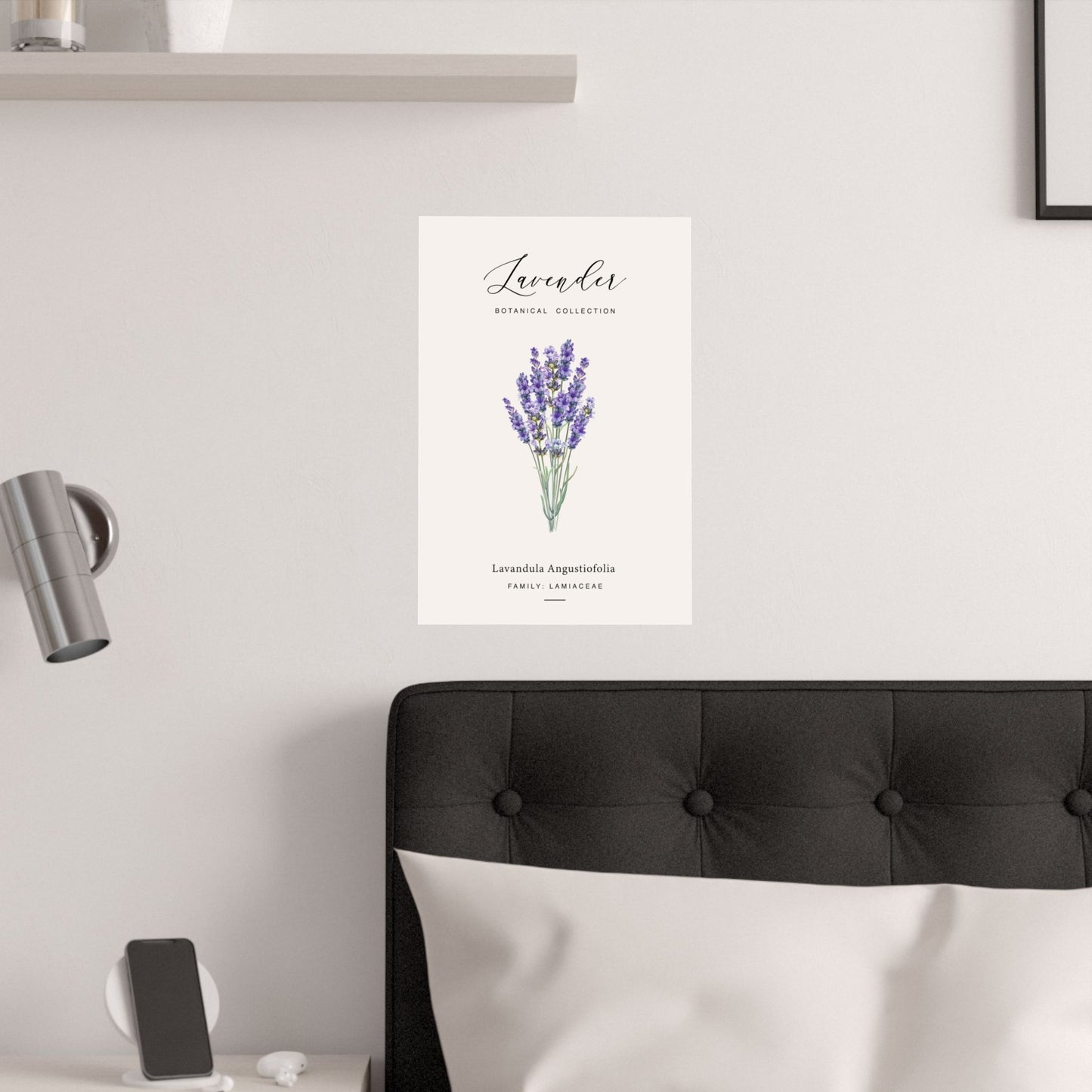 Lavender botanical poster hung on a white wall above a black upholstered bed with white bedding and a wall-mounted spotlight
