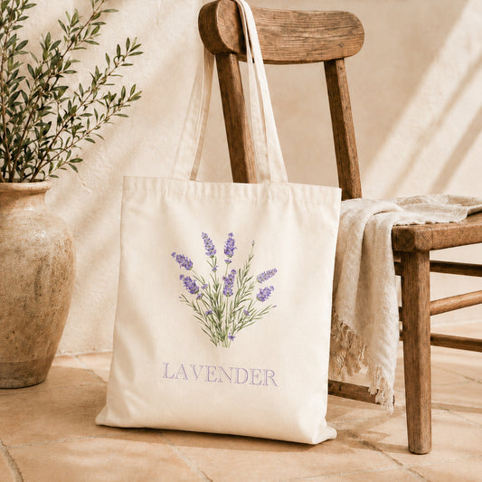 Natural canvas tote bag with purple lavender botanical print resting on a wooden chair beside an olive plant in a terra cotta pot