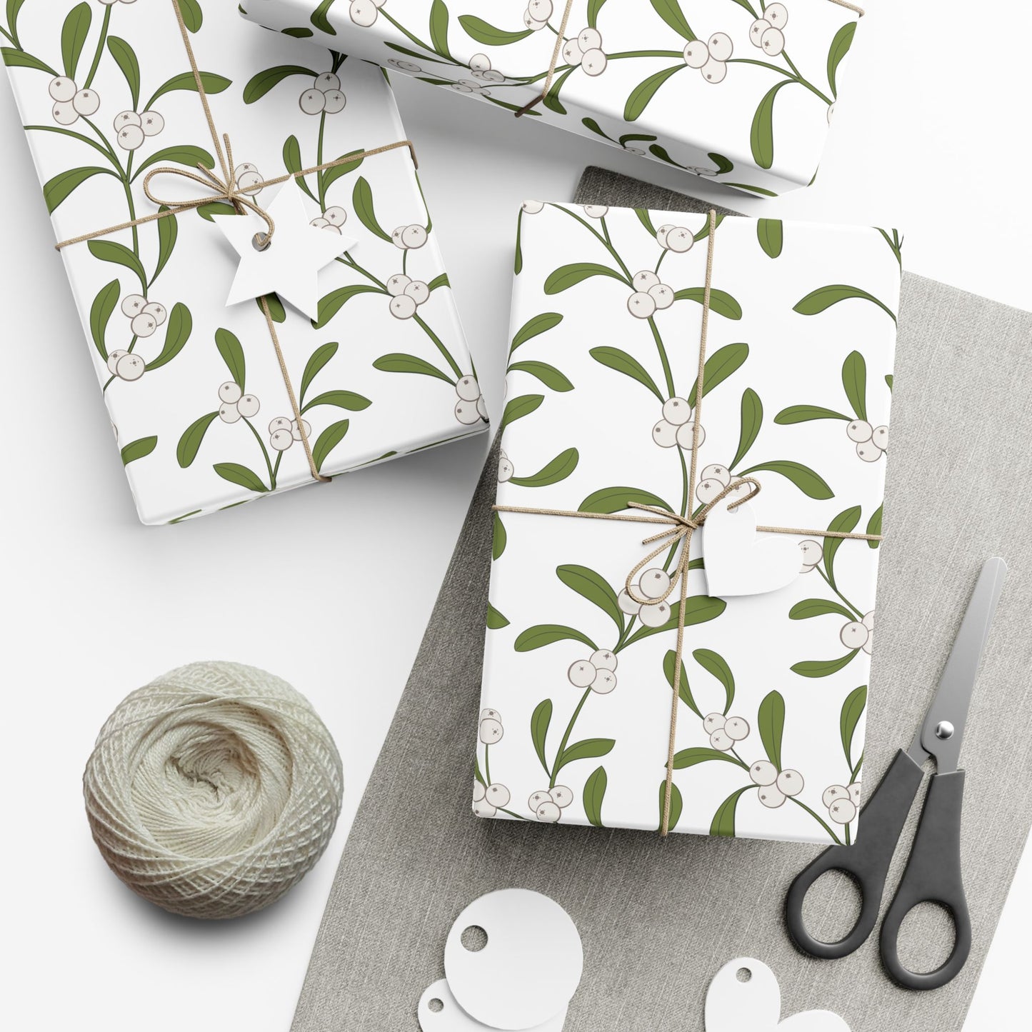 Two gifts wrapped in mistletoe pattern paper with round tags and scissors on linen