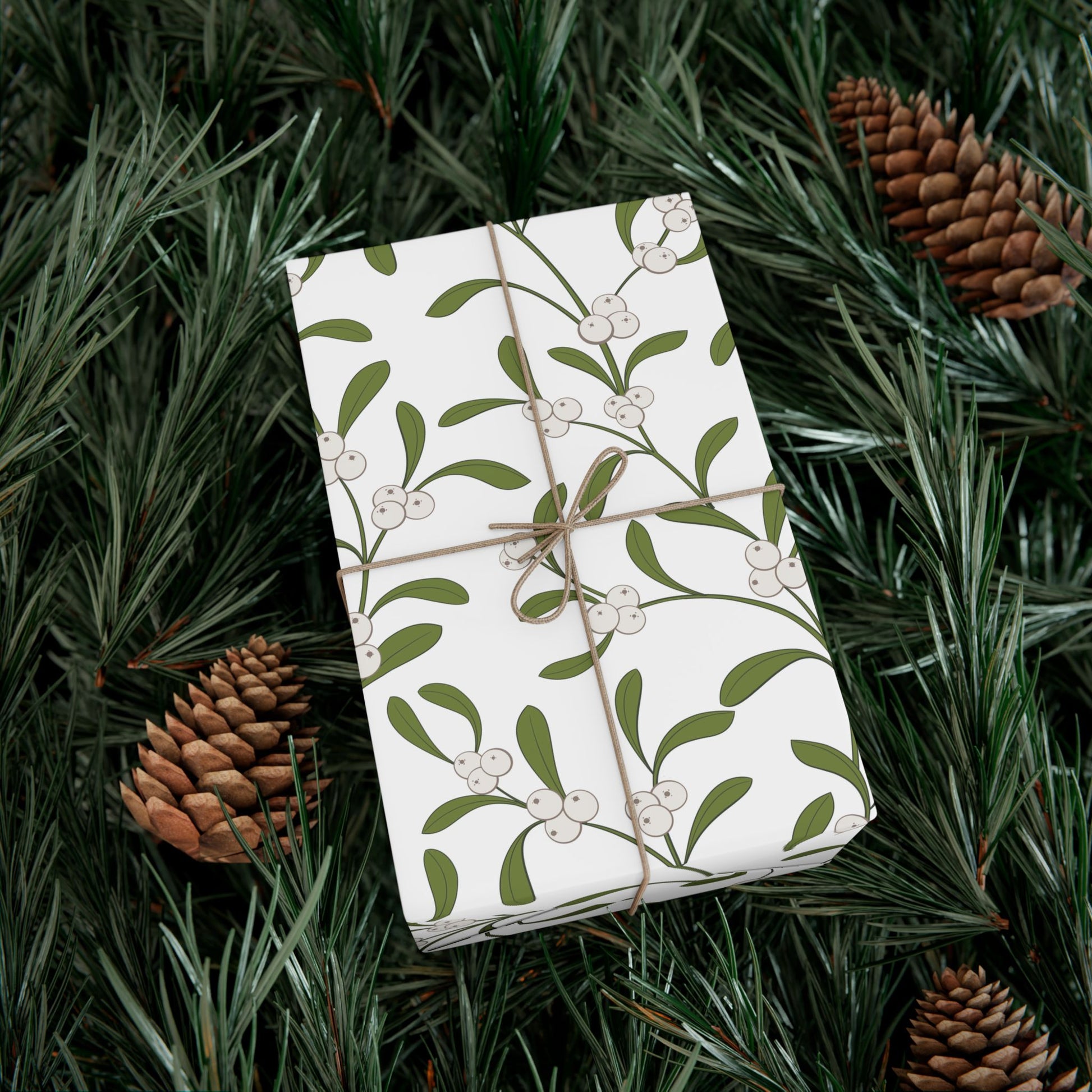 Gift wrapped in mistletoe pattern paper on pine branches with pinecones