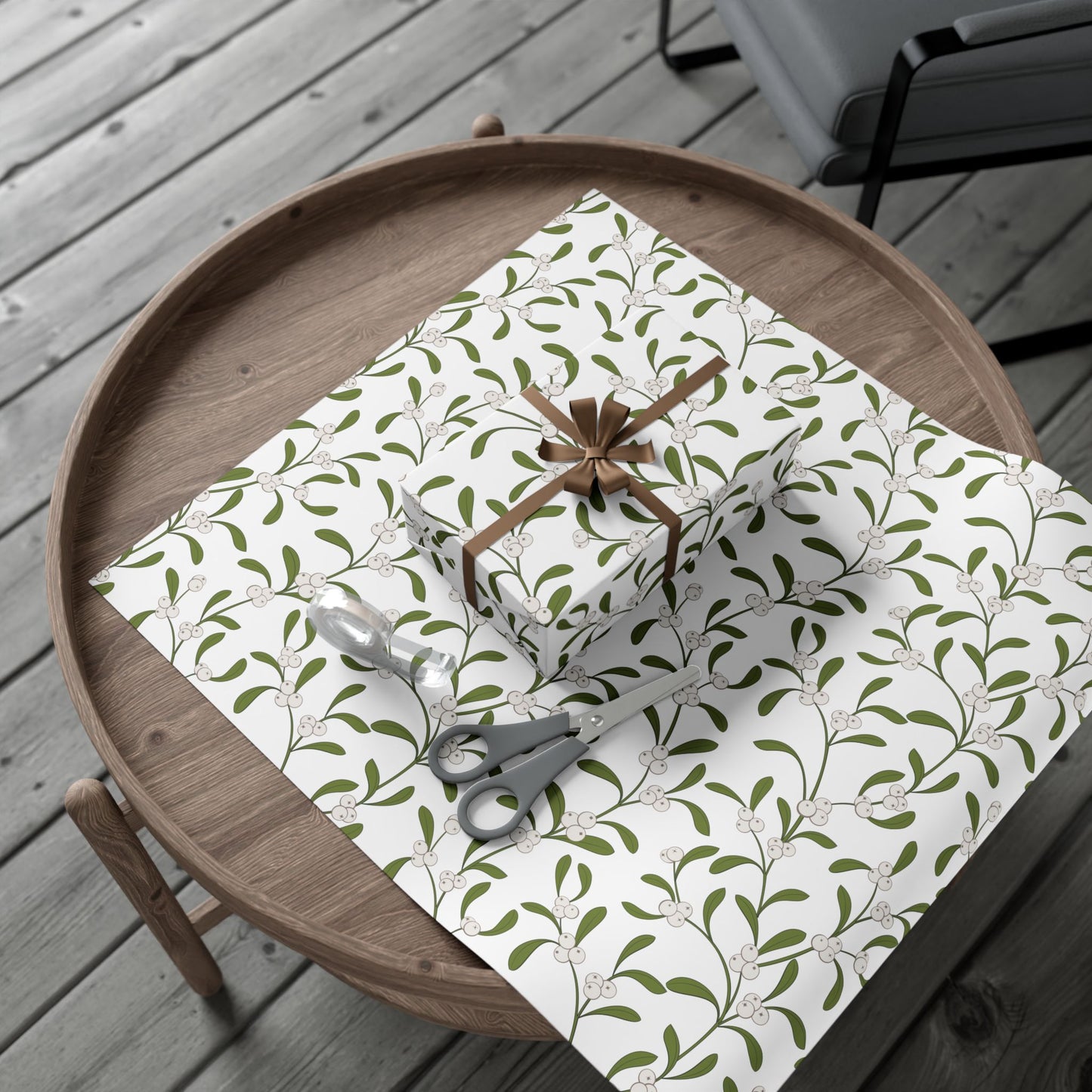 Mistletoe pattern gift wrap roll and wrapped gift with bow on a round wood table