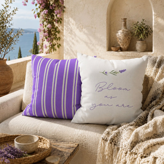 Lavender stripe and botanical text decorative pillows displayed on a cream outdoor sofa beside woven baskets and flowering vines on a Mediterranean patio